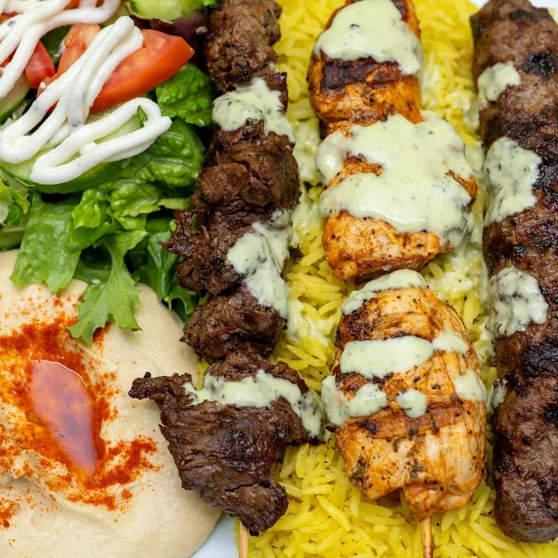 Mixed grill plate: beef, chicken and kofta kabobs over rice with hummus and salad